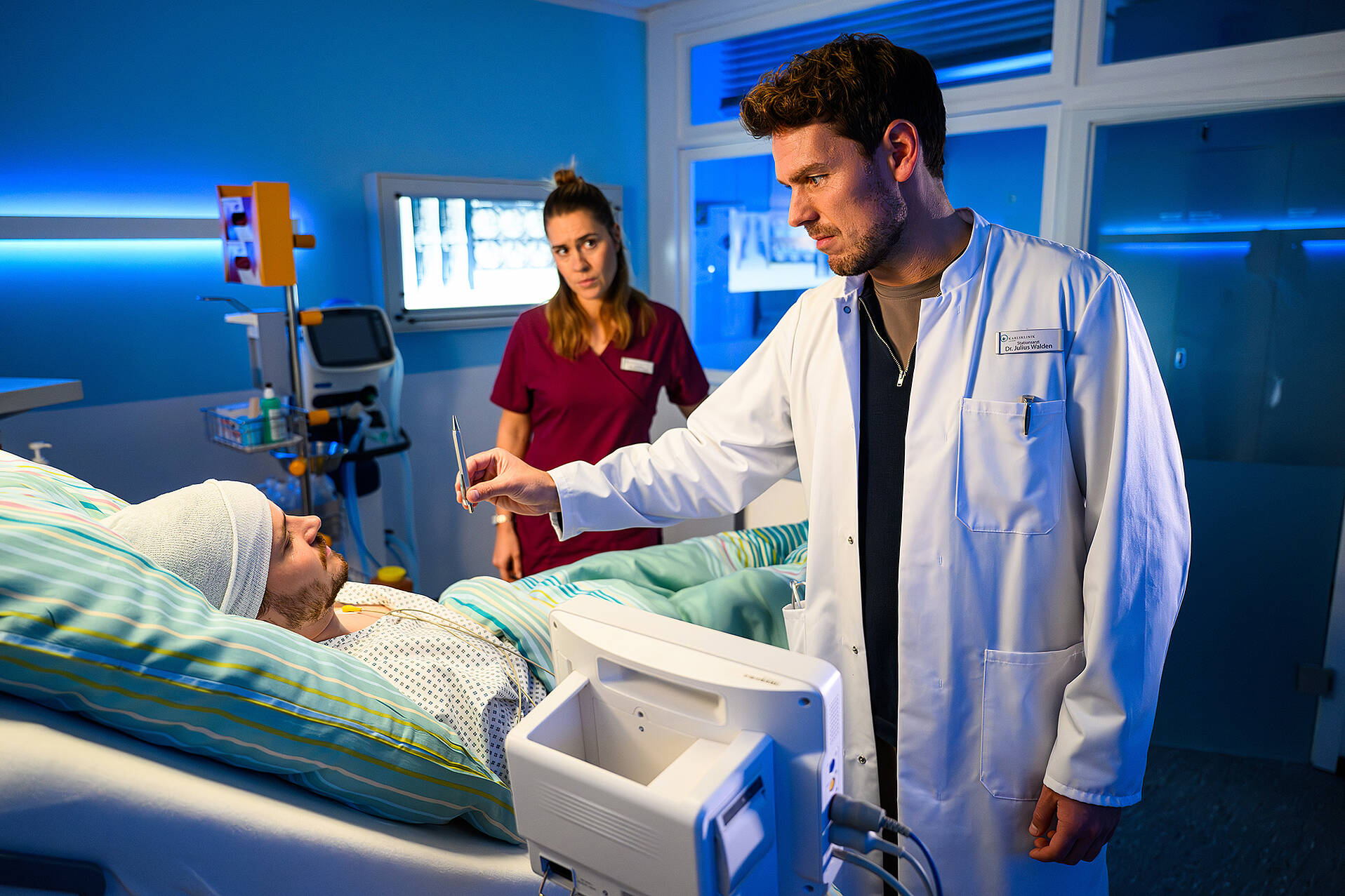 Dr. Julius Walden (Constantin Lücke) und Elisabeth Herz (Henrike Hahn) stehen am Krankenbett von Aaron Behrends (Tilman Pörzgen) (© ZDF/Willi Weber)